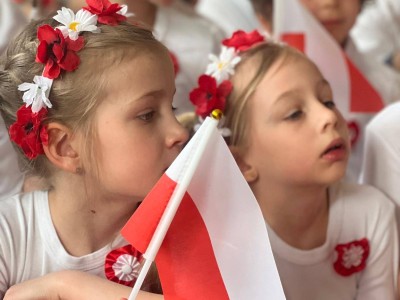 Dziewczynka trzyma flagę Polski i i ma wianek z kwiatów na głowie