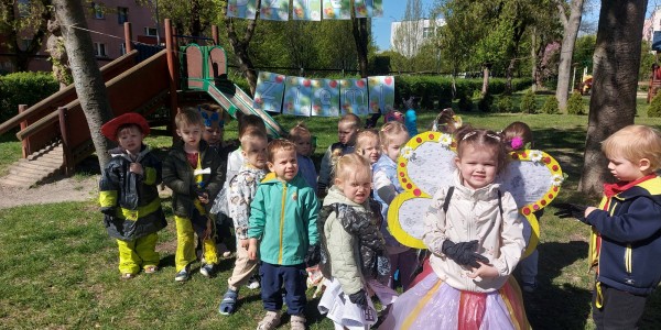 Grupa przedszkolaków w parku podczas akcji sprzątania, dziewczynka w żółtych skrzydłach pszczoły, chłopcy w odblaskowych kami