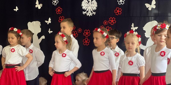 Grupa dzieci w strojach biało-czerwonych na scenie podczas uroczystości.