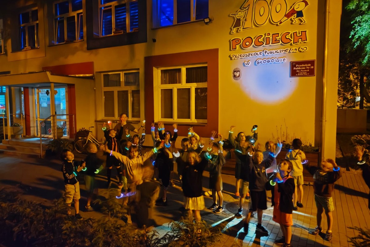 Grupa dzieci z świecącymi opaskami bawi się nocą przed budynkiem Przedszkola Publicznego Nr 10 Sto Pociech w Głogowie.