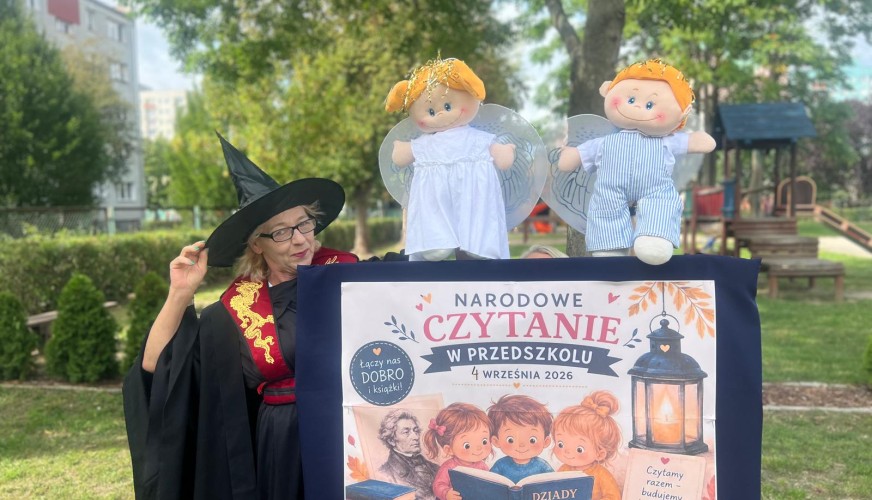 Nauczycielka w stroju czarownicy stoi przy stole z banerem Narodowe Czytanie w Przedszkolu 4 września 2026 i dwoma lalkami an