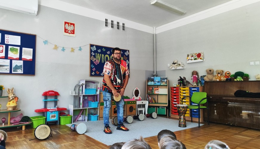 Mężczyzna w kolorowej koszuli trzyma bęben djembe przed grupą dzieci
