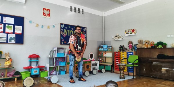 Mężczyzna w kolorowej koszuli trzyma bęben djembe przed grupą dzieci