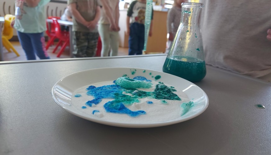 Biały talerz z niebiesko-zielonymi plamami barwnika, obok szklanka z zielonym płynem.