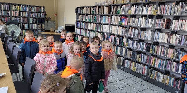 Grupa około 20 dzieci w pomarańczowych kamizelkach odblaskowych.