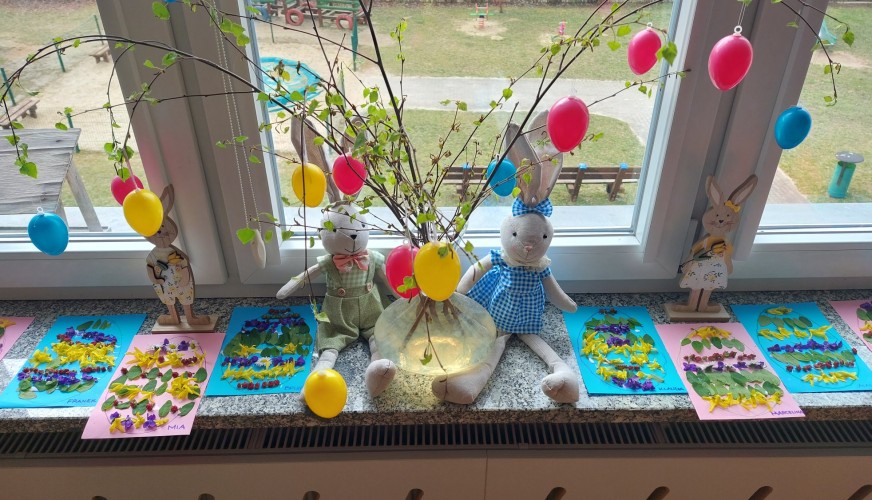 Dekoracja świąteczna na parapecie: gałęzie z kolorowymi balonami, trzy pluszowe króliki w sukienkach, artystyczne prace